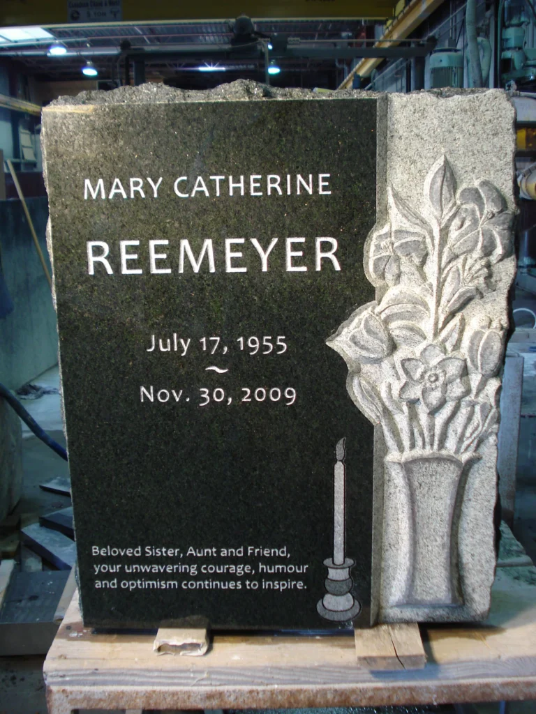 A black granite tombstone with sculpted lilies and a candle